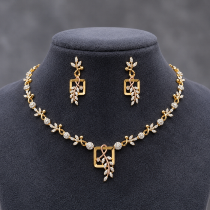 Gold jewelry set featuring a necklace and matching drop earrings displayed on a dark gray velvet jewelry bust. The set features gold square motifs and leaf-like details set with clear stones.