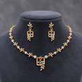 Gold jewelry set featuring a necklace and matching drop earrings displayed on a dark gray velvet jewelry bust. The set features gold square motifs and leaf-like details set with clear stones.