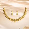 Gold jewelry set featuring a curved necklace and matching drop earrings with green floral engravings, displayed on a beige satin fabric background with small white flowers.