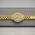 A gold-tone Mercedes-Benz watch with a diamond-encrusted bezel and matching diamond-embellished bracelet, displayed on a gray textured watch box.