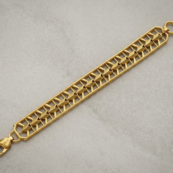A gold-toned metal link bracelet with a geometric, openwork trellis pattern, featuring a lobster clasp and a top loop, shown on a textured light gray background.