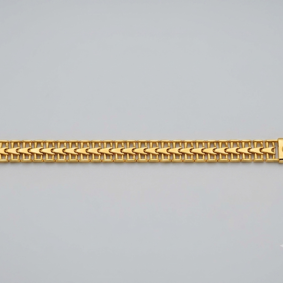 A gold-colored metal link bracelet with a woven chevron pattern, displayed horizontally against a neutral light gray background.