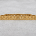 A gold-tone metal bracelet with a textured honeycomb pattern and small clear stones set along the top, displayed on a light gray textured background.