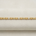 A yellow gold link bracelet with diamond-shaped diamond-cut links and a small turquoise accent on the clasp, displayed on a cream-colored textured surface.