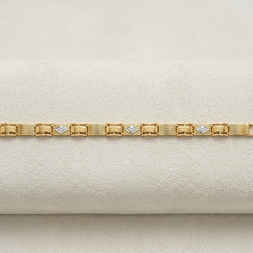 A yellow gold link bracelet with diamond-shaped diamond-cut links and a small turquoise accent on the clasp, displayed on a cream-colored textured surface.