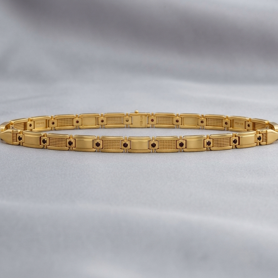 A gold link bracelet with a segmented, geometric design featuring textured and polished rectangular links, displayed on a soft, draped gray fabric background.