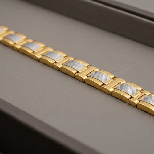 A close-up of a gold-tone metal link bracelet with textured silver inlay panels, resting diagonally on a dark gray textured surface.