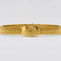 A gold-tone metal link bracelet watch band with a central oval plate featuring a crown emblem, photographed against a clean light gray background.