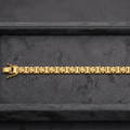 A gold link bracelet with a distinctive bow-shaped clasp, displayed horizontally on a dark gray velvet jewelry box.