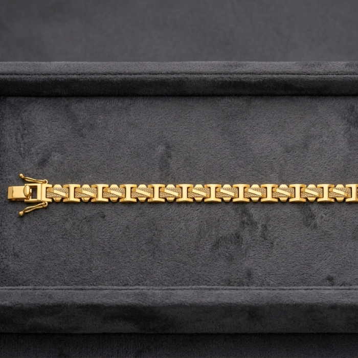 A gold link bracelet with a distinctive bow-shaped clasp, displayed horizontally on a dark gray velvet jewelry box.