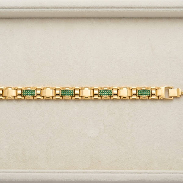 A gold link bracelet with green and pink pavé accents, displayed horizontally on a light beige textured jewelry box.