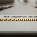 A gold-colored metal link bracelet laid horizontally on a gray textured surface, with blurred jewelry tools in the background. White text across the center reads 'WEIGHT--16GM LENTH-8" WIDTH--10MM 22KT' and a small code 'FGB-048' appears on the right.