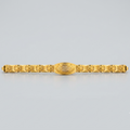 A gold-plated metal bracelet with a central oval medallion and repeating geometric links on either side, shown against a light gray background.