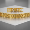 A gold link bracelet displayed on a brushed metal pedestal against a soft gray background.
