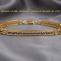 A gold-plated S-shaped bracelet with a central bar set with small dark stones, displayed on a gray fabric background with gold-colored text overlay detailing its specifications.