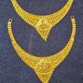 A pair of gold crescent-shaped traditional Indian jewelry pieces, likely waist chains or decorative necklaces, displayed on a dark textured background.
