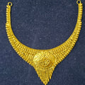 A gold-toned traditional necklace with intricate filigree patterns and a central medallion, displayed on a dark textured background.