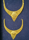 A pair of ornate gold-toned necklace pendants displayed on a dark blue velvet jewelry box insert.