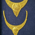 A pair of ornate gold-toned traditional necklace pieces displayed on a dark navy velvet jewelry box insert.