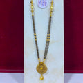 A gold and black beaded necklace with a round gold pendant, displayed on a white jewelry stand against a dark red background.