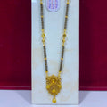 A traditional Indian gold necklace with black beads and a large ornate gold pendant, displayed on a white stand against a dark red background.