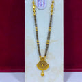 A traditional Indian gold necklace with a black bead chain and a detailed gold pendant, displayed on a white stand against a red background.