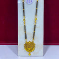 A gold and black beaded necklace with a detailed gold pendant, displayed on a white stand against a dark red background.