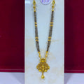 A traditional Indian gold and black beaded necklace with a detailed gold pendant, displayed on a white stand against a red background.