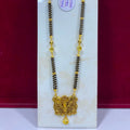 A traditional Indian gold and black beaded necklace with a detailed gold pendant, displayed on a white marble stand against a dark red background.