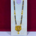 A gold and black beaded necklace displayed on a white stand against a dark red background. The necklace features a detailed gold pendant with elephant motifs and a teardrop charm at the bottom.
