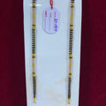 Two gold and black beaded bracelets on a white stand with a red background