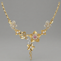 An ornate gold floral necklace with diamond accents and a central pink gemstone, displayed on a neutral gray background.