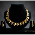 Gold-toned jewelry set displayed on a black velvet bust, including a necklace with leaf-shaped elements and matching drop earrings, shown against a dark gray studio background. A small text box at the bottom right reads 'gold wt = 17.