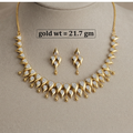 Gold-tone jewelry set displayed on a beige mannequin bust, including a necklace and matching earrings with clear teardrop-shaped stones. A text label reads 'gold wt = 21.