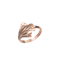 A rose gold ring with a sculptural, layered petal-like design and small clear gemstones, shown on a plain white background with a product code label in the bottom left and an 'DC' logo below.