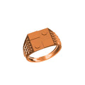 A rose gold signet ring with a geometric, block-like face featuring circular cutouts and textured sides, shown on a plain white background with a small catalog label and 'DC' logo at the bottom.