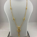 A gold necklace displayed on a white jewelry bust, with a digital scale visible underneath. The necklace features a delicate chain with small bead details and a central key-shaped pendant.