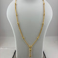 A gold necklace displayed on a white jewelry bust, with a digital scale visible underneath. The necklace features a delicate chain with small bead-like links and a central pendant with a tassel drop.