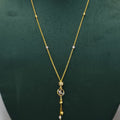 A gold chain necklace with a circular pendant and dangling tassels, displayed on a dark green velvet jewelry bust against a light gray background.