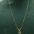 A gold necklace with a small circular pendant displayed on a dark green jewelry bust against a light gray background.