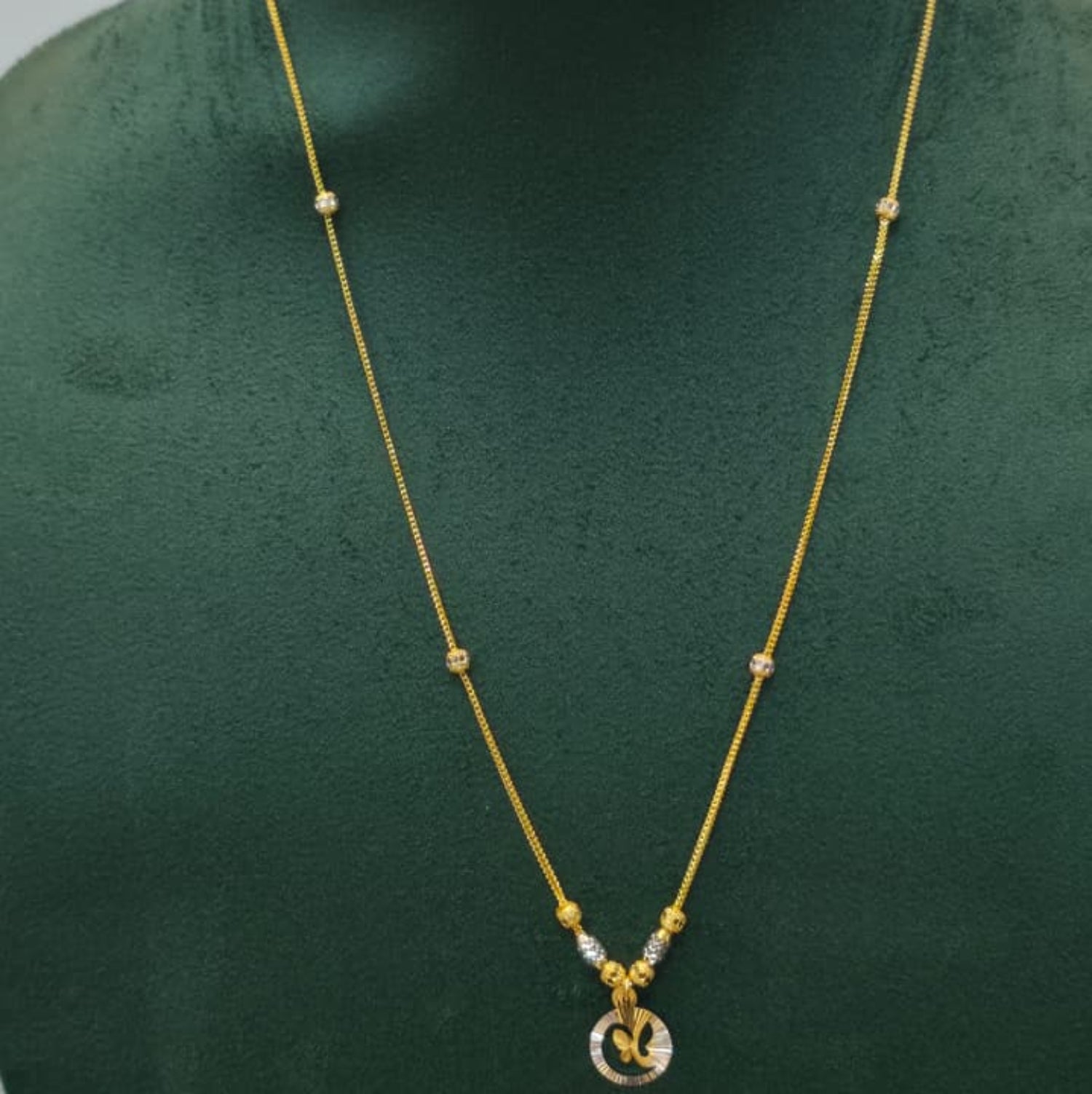 A gold necklace with a small circular pendant displayed on a dark green jewelry bust against a light gray background.