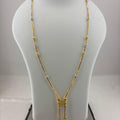 A gold necklace displayed on a white mannequin bust, with a digital scale visible underneath. The necklace features a Y-shaped design with small silver-toned bead accents and a central gold pendant with dangling chains.