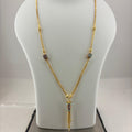 A gold necklace with a tassel pendant and small colorful stone accents, displayed on a white jewelry bust scale on top of a digital scale showing 9.92 grams.