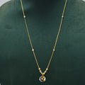 A delicate gold chain necklace with small bead accents and a round pendant, displayed on a dark green jewelry bust against a light gray background.