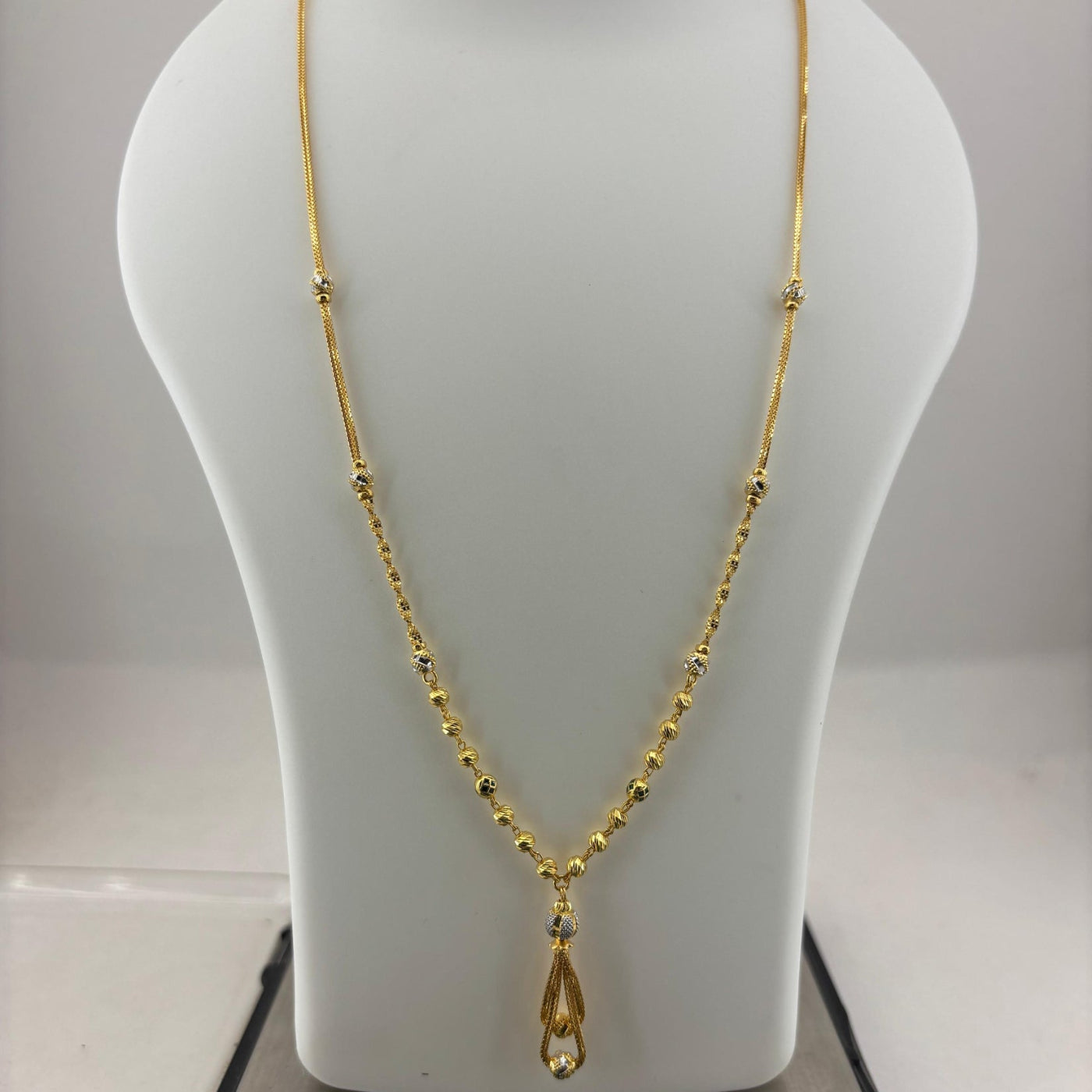 A gold chain necklace with a teardrop-shaped pendant displayed on a white jewelry bust, with a digital scale visible underneath.