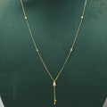 A delicate gold necklace with a central teardrop-shaped pearl and a dangling gold charm, displayed on a dark green jewelry bust.
