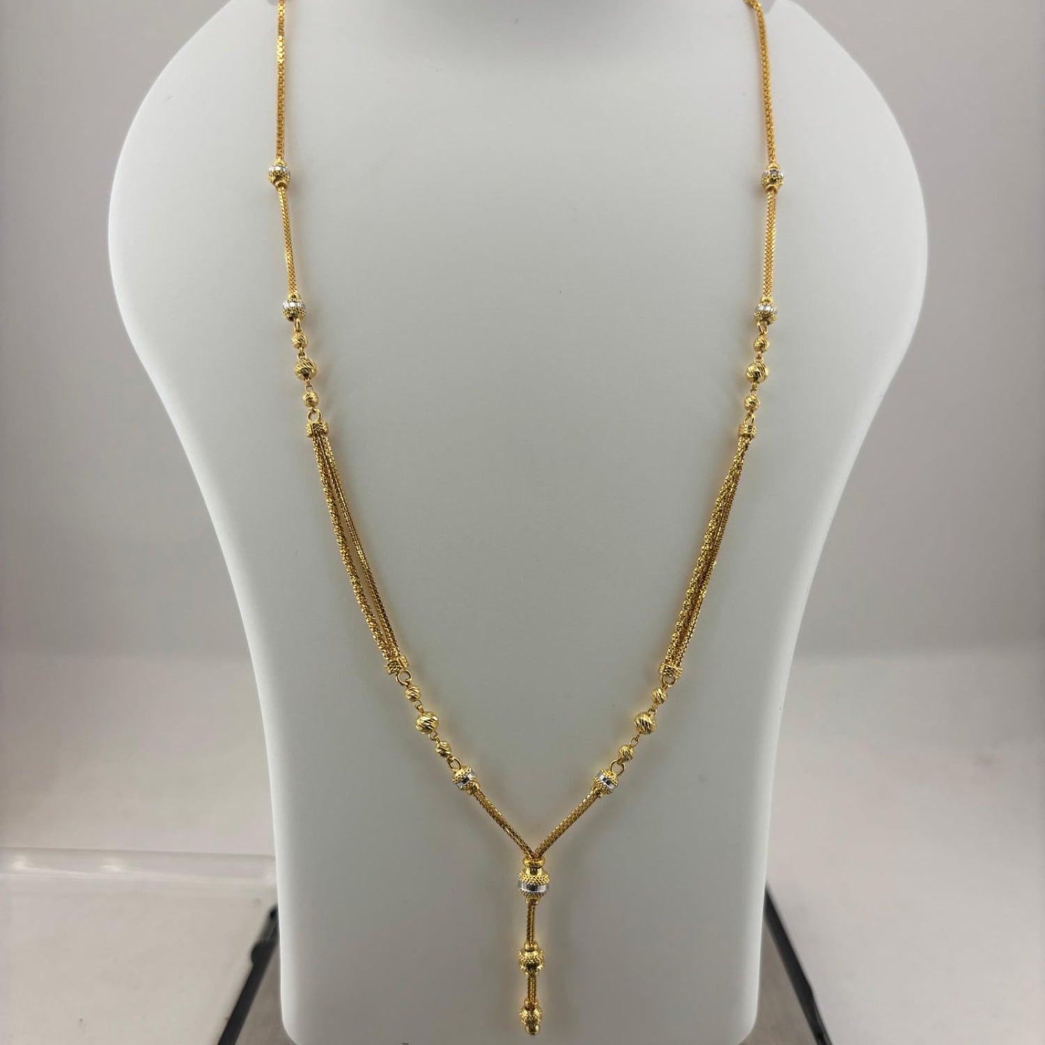 A gold necklace displayed on a white mannequin bust, with a digital scale visible underneath.