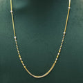 A delicate gold chain necklace with small silver bead accents, displayed on a dark green jewelry bust.