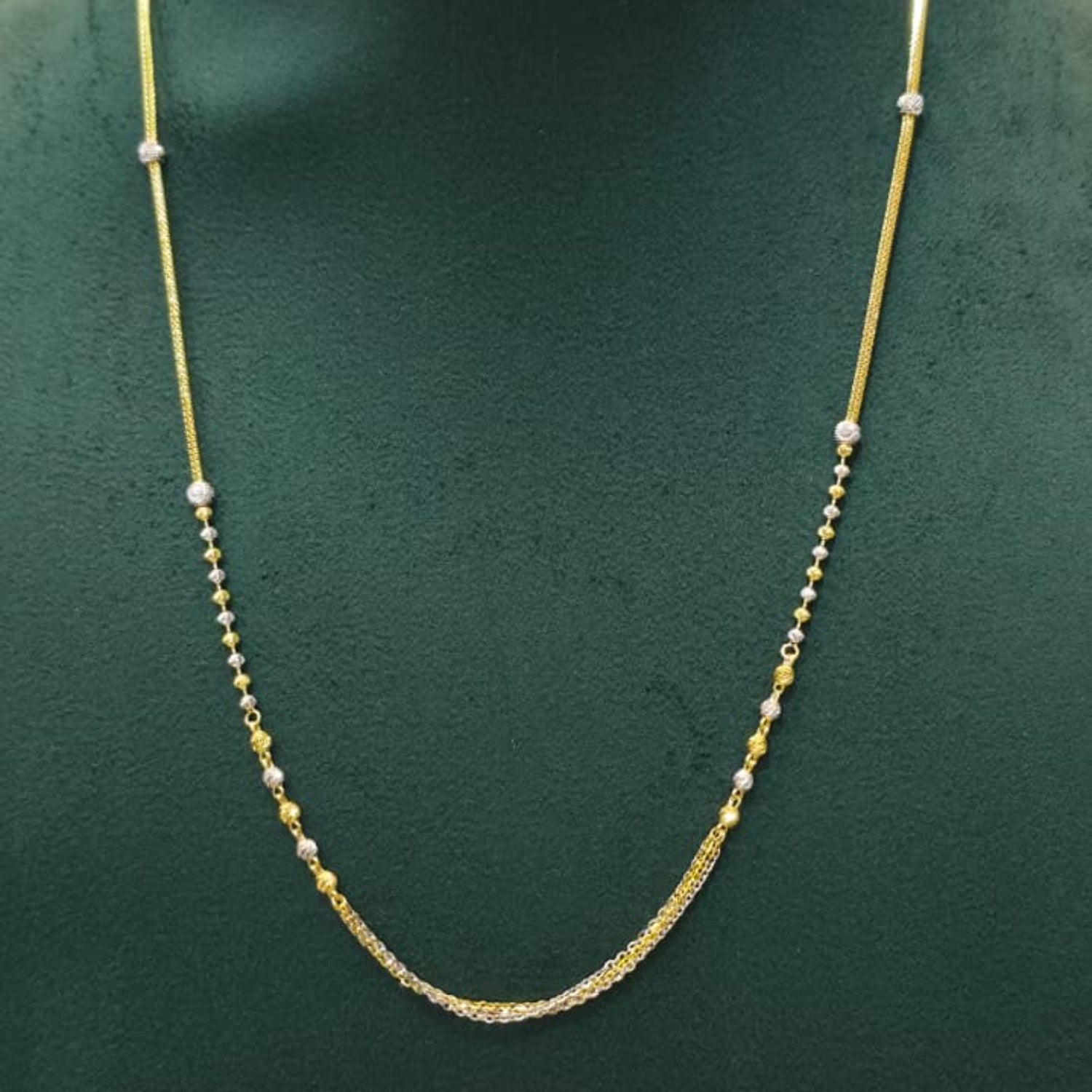 A delicate gold chain necklace with small silver bead accents, displayed on a dark green jewelry bust.