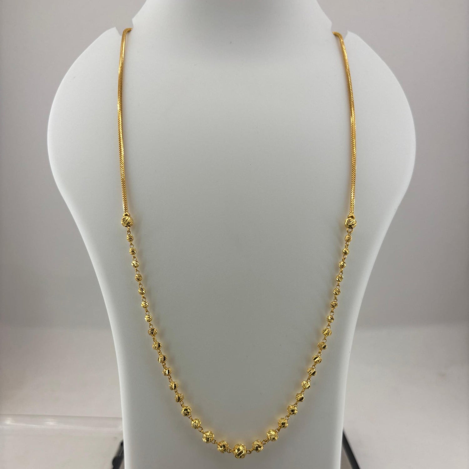 A gold chain necklace displayed on a white mannequin bust, with a digital scale visible underneath.